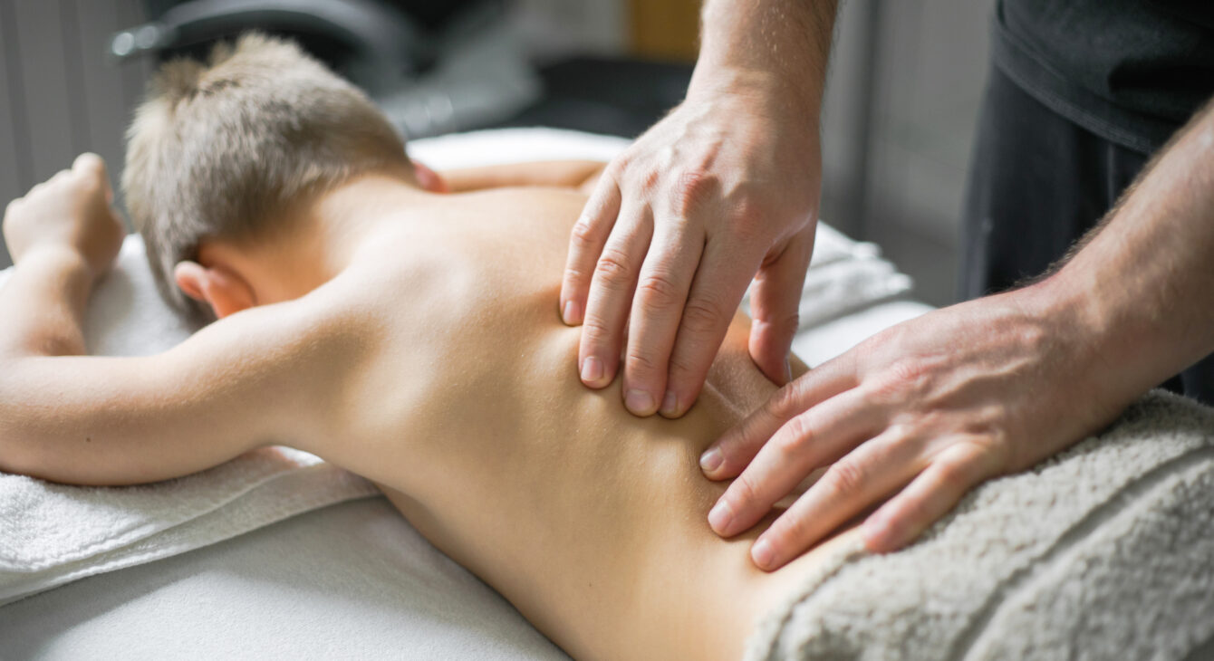 Professional  Physiotherapist is treating a kid in clinic. Boy toddler relaxes from a therapeutic massage.